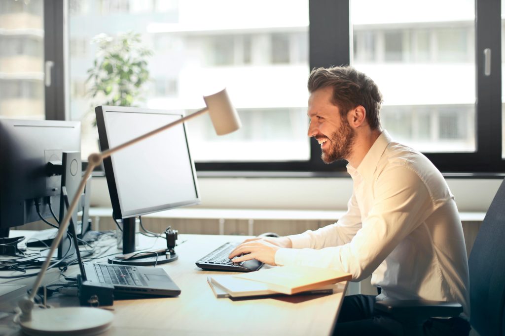 pexels-photo-840996-840996 Man in White Dress Shirt Sitting on Black Rolling Chair While Facing Black Computer Set and Smiling